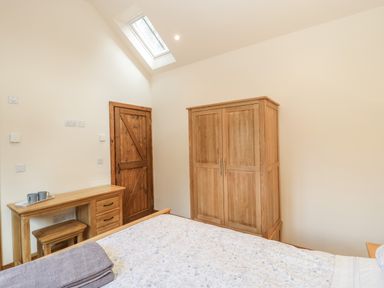 A bedroom with a wooden wardrobe a wooden desk with stools a wooden door and a skylight at The Milking Barn in Yeovil Somerset