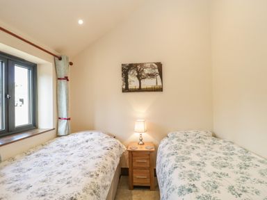 A bedroom with two single beds a window and a nightstand with a lamp at The Milking Barn in Yeovil Somerset