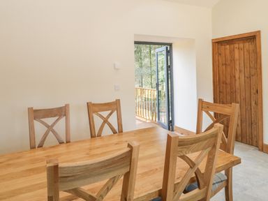 A dining room with a wooden table and chairs next to a wooden door and an open door leading outside at The Milking Barn in Yeovil Somerset