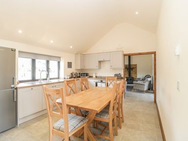 A kitchen with wooden dining table and six chairs next to cabinets and a window at The Milking Barn in Yeovil Somerset