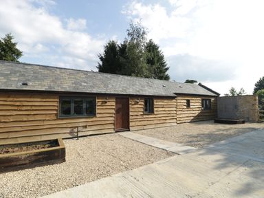 A single-story building with wooden cladding and multiple windows on a gravel ground at The Milking Barn in Yeovil Somerset