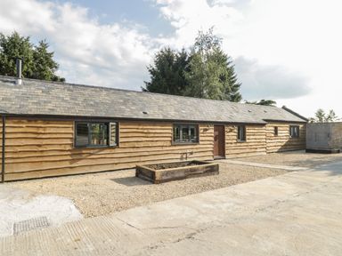 A single-story wooden building with a slate roof and multiple windows with gravel and concrete in front at The Milking Barn in Yeovil Somerset