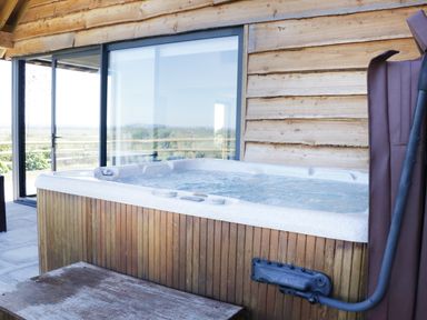 An outdoor hot tub with wooden siding next to a wooden cabin with sliding glass doors at Heron Lodge Castle Farm in Wedmore