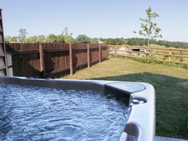 An outdoor hot tub with water bubbling near a wooden fence and grassy area at Heron Lodge Castle Farm in Wedmore