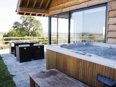 An outdoor patio area with a hot tub and dining table with chairs at Heron Lodge Castle Farm in Wedmore