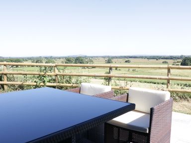 A patio table and two chairs overlooking fields with a wooden fence at Heron Lodge Castle Farm in Wedmore