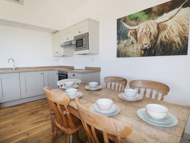 A kitchen with wooden flooring a wooden dining table set with bowls and plates wooden chairs cupboards and a framed picture of a highland cow on the wall at Heron Lodge Castle Farm in Wedmore