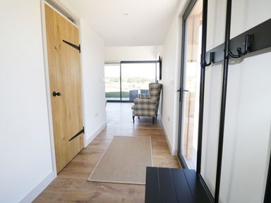 A hallway with a wooden door a rug a coat rack and a plaid armchair at Heron Lodge Castle Farm in Wedmore