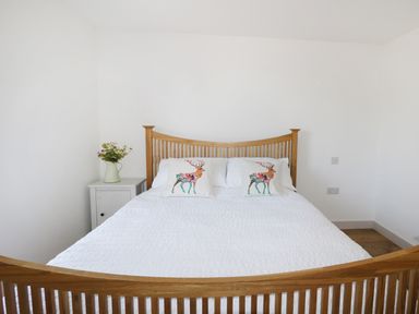 A bedroom with a wooden bed frame white bedding two pillows with deer prints and a nightstand with flowers at Heron Lodge Castle Farm in Wedmore