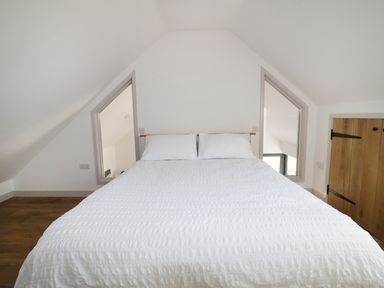A bedroom with a white bed and two windows on a sloped ceiling wall at Heron Lodge Castle Farm in Wedmore