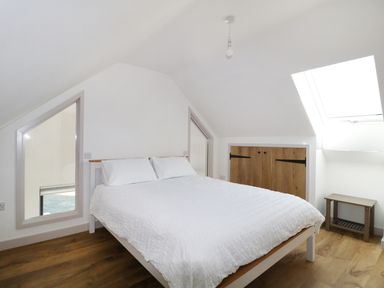 A bedroom with a bed two pillows a skylight window wooden floor and a small wooden table at Heron Lodge Castle Farm in Wedmore