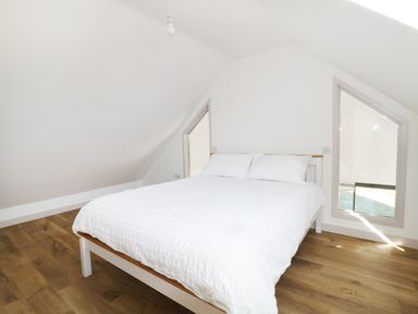 A bedroom with a bed with white bedding under a sloped ceiling with a window at Heron Lodge Castle Farm in Wedmore
