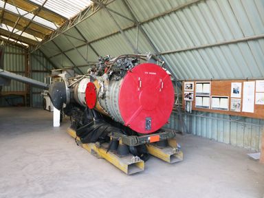An aircraft engine with red covers inside a metal hangar with a bulletin board on the wall at Heron Lodge Castle Farm Wedmore