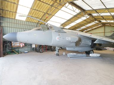 A gray military jet aircraft inside a metal hangar with various items on the ground at Heron Lodge Castle Farm in Wedmore