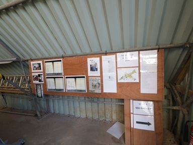 A bulletin board with papers and images attached inside a corrugated metal structure at Heron Lodge Castle Farm in Wedmore