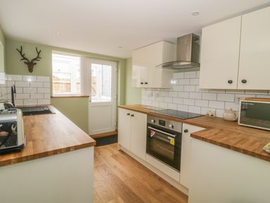A kitchen with wood countertops white cabinets an electric stove a toaster a microwave and a door with a window at 2 Hillside Cottages in Felixstowe Suffolk