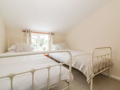 A bedroom with two single beds a window with plaid curtains and a bedside table with a lamp at 2 Hillside Cottages Felixstowe Suffolk