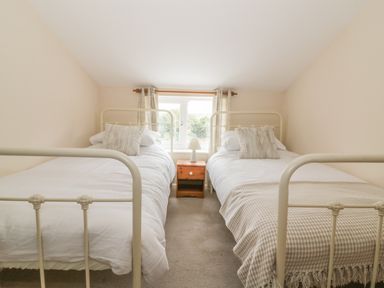 A bedroom with two single beds separated by a wooden nightstand with a lamp at 2 Hillside Cottages in Felixstowe Suffolk