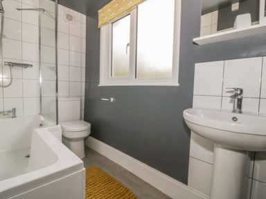A bathroom with a bathtub shower toilet sink window and yellow bath mat at 2 Hillside Cottages in Felixstowe Suffolk