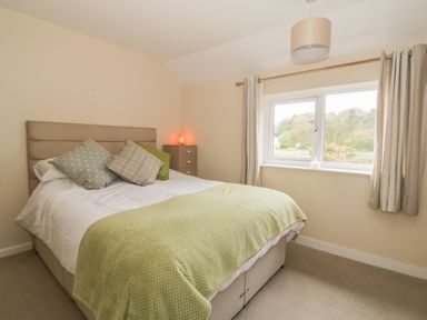 A bedroom with a bed with green throw and pillows and a window with curtains at 2 Hillside Cottages in Felixstowe Suffolk