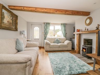 A living room with two sofas a blue rug wood flooring a fireplace and window curtains at 2 Hillside Cottages in Felixstowe Suffolk