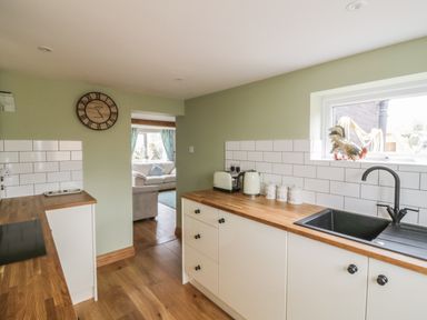A kitchen with wooden countertops white cabinets a black sink and appliances visible through an open doorway at 2 Hillside Cottages Felixstowe Suffolk