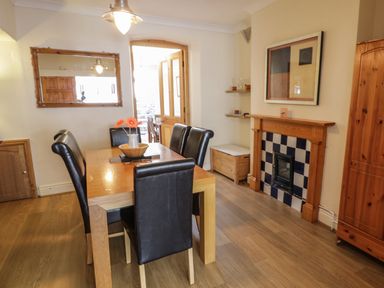 A dining room with a wooden table and black chairs a fireplace with blue and white tiles and a wooden cabinet at Chwech in Menai Bridge
