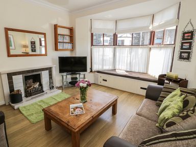 A living room with a fireplace a wooden coffee table a sofa and a bay window seat at Chwech in Menai Bridge