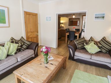 A living room with two sofas a wooden coffee table with flowers and a view into a dining area at Chwech in Menai Bridge