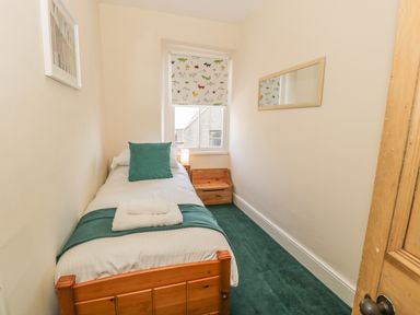 A small bedroom with a single wooden bed a green cushion towels on the bed a window with animal patterned blind and a wooden chest at Chwech in Menai Bridge