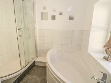 A bathroom with a corner bathtub and a glass shower enclosure with tiled walls at Chwech in Menai Bridge