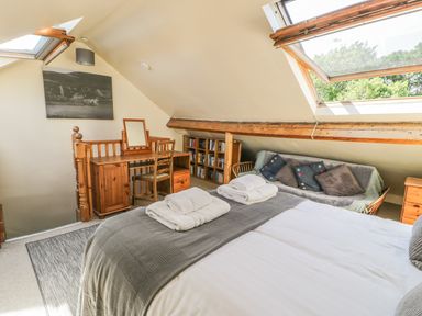 A bedroom with a bed, wooden desk, chair, bookshelf, couch with cushions, and large skylight window at Chwech in Menai Bridge