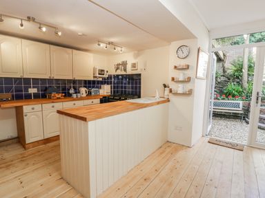 A kitchen with wooden countertops white cabinets blue tiled backsplash and glass door leading to garden at Chwech in Menai Bridge