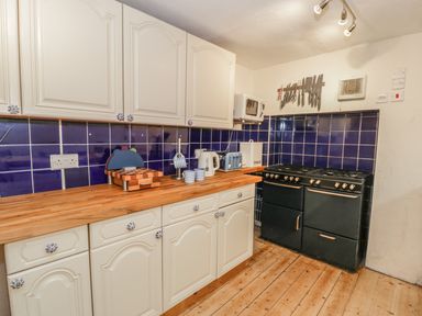 A kitchen with white cabinets blue tiled backsplash wooden countertop black stove and kitchen utensils at Chwech in Menai Bridge