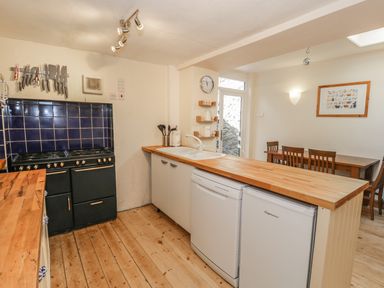 A kitchen with a wooden countertop a black stove knives on a wall mounted rack and a dining table with chairs at Chwech in Menai Bridge