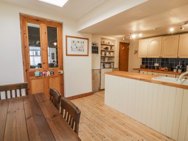 A kitchen with wooden dining table chairs a wooden door white cabinets and shelves with dishes at Chwech in Menai Bridge