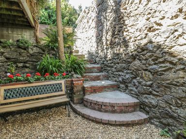 An outdoor stone stairway beside a stone wall with a bench and plants at Chwech in Menai Bridge