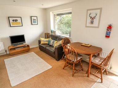A living room with a leather sofa a wooden dining table with three chairs a television on a wooden stand and framed pictures on the walls at Latterbarrow in Hawkshead
