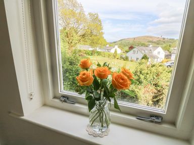 A vase with orange roses on a windowsill with a view of houses and trees at Latterbarrow in Hawkshead