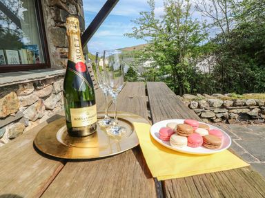 A wooden picnic table with a bottle of champagne two glasses and a plate of macarons outdoors at Latterbarrow in Hawkshead