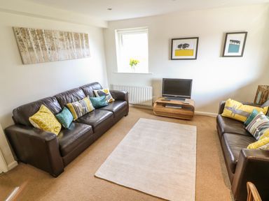 A living room with two brown leather sofas a small wooden TV stand with a television and framed pictures on the wall at Latterbarrow in Hawkshead