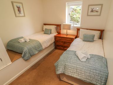 A bedroom with two single beds a wooden nightstand with a lamp between them and framed pictures on the walls at Latterbarrow in Hawkshead