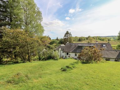 A house with a dark roof surrounded by grass and trees with hills in the background at Latterbarrow in Hawkshead