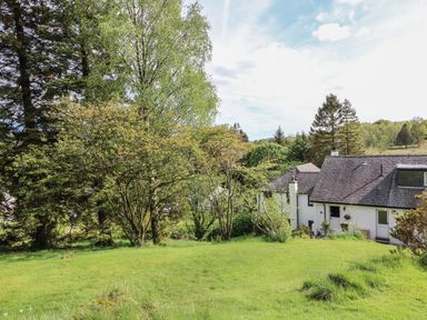 A grassy yard with trees surrounding a white house with a slate roof at Latterbarrow in Hawkshead