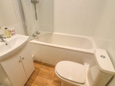 A bathroom with a bathtub shower combination a toilet and a sink with cabinets at Latterbarrow in Hawkshead