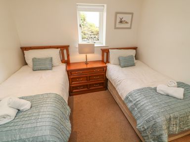 A bedroom with two single beds a wooden nightstand lamp and a window at Latterbarrow in Hawkshead
