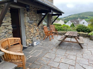 A stone patio with wooden chairs a picnic table and potted plants outside a stone building at Latterbarrow in Hawkshead