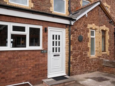 The exterior of a brick and stone house with a white door and windows at 4 High Bank