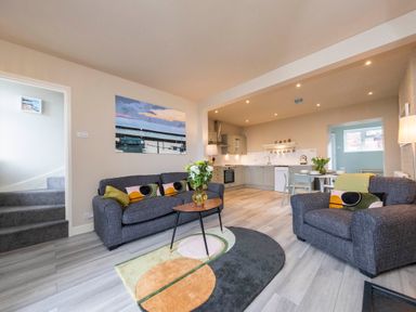 An open plan living room and kitchen with sofas a round table and a colorful rug at Harbour View Cottage in Watchet