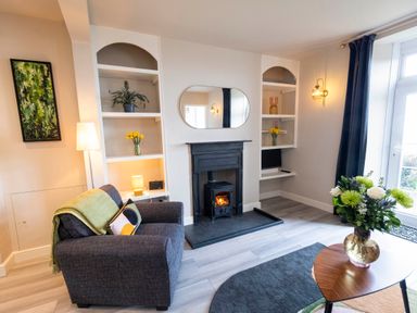 A living room with a fireplace armchair flowers and shelves at Harbour View Cottage in Watchet